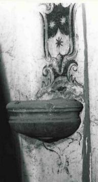 ::Acquasantiera ovale, in marmo grigio, 
addossata alla parete, dove  dipinta uno stemma::